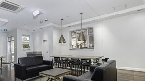 Un área de descanso moderna con sofá, sillas, una mesa baja de madera e iluminación colgante.