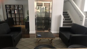 Un vestíbulo moderno con sofás de cuero negro, una mesa de centro de madera y una escalera.