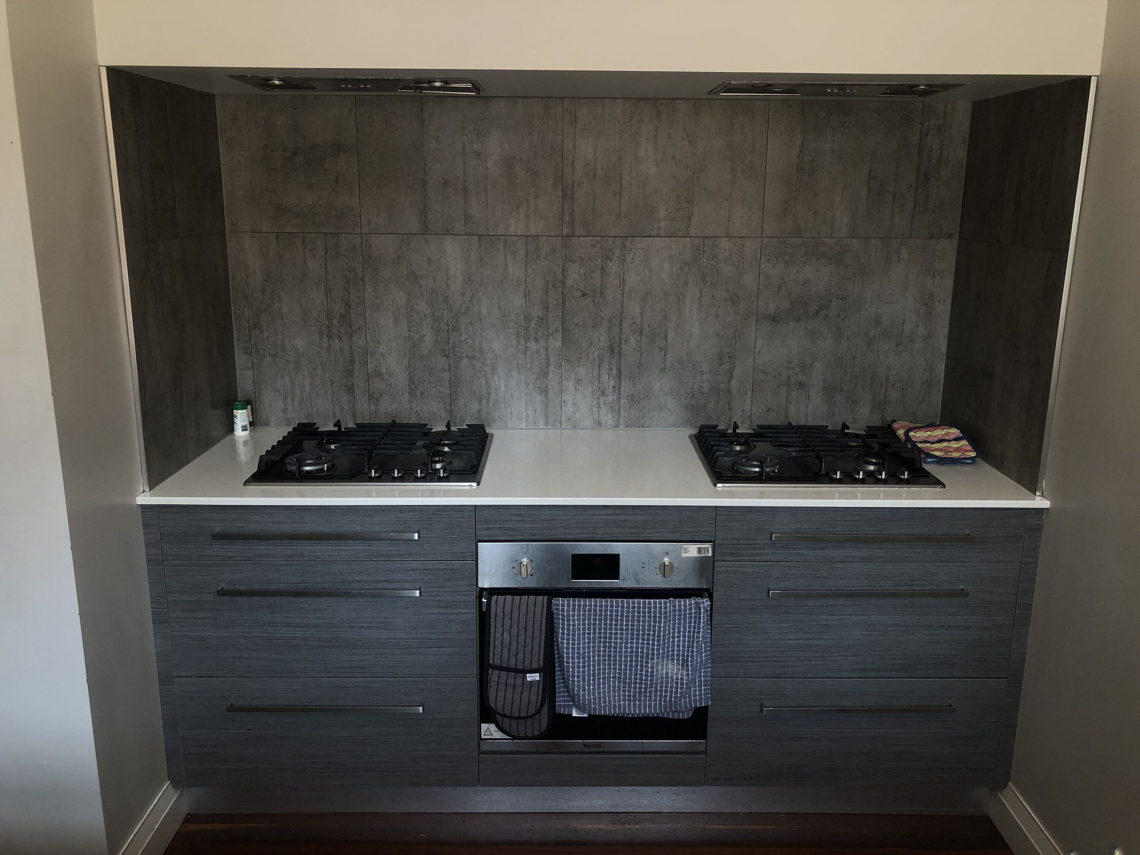 A modern kitchen with two gas stoves, a built-in oven, and a stainless steel backsplash.