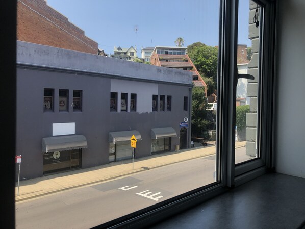 Vista a través de una ventana de un edificio de fachada gris, con numerosas ventanas y toldos.
