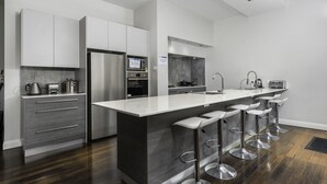 Una cocina moderna con una isla central, taburetes de bar, electrodomésticos de acero inoxidable y una paleta de colores gris y blanco.