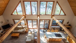 A spacious loft with a high ceiling, large windows, a cozy seating area, and a dining space. - Lakefront cabin on Minong Flowage (Minong)