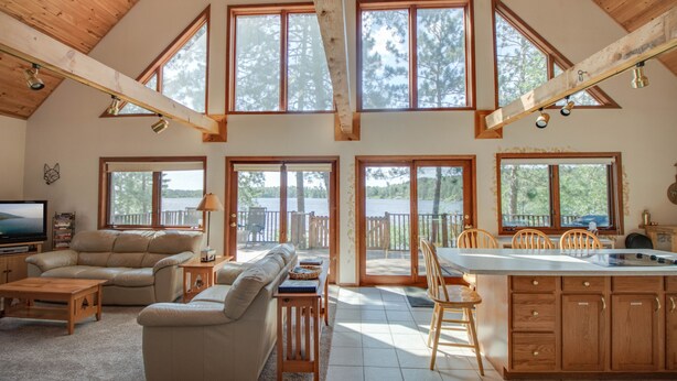 A spacious living area with a high ceiling, large windows, and a kitchen with wooden cabinets. - Lakefront cabin on Minong Flowage (Minong)