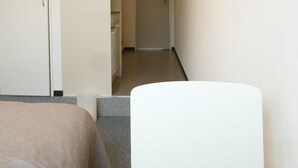 Ein schmaler Flur mit einem Bett, einem weißen Stuhl und einer Tür am Ende.