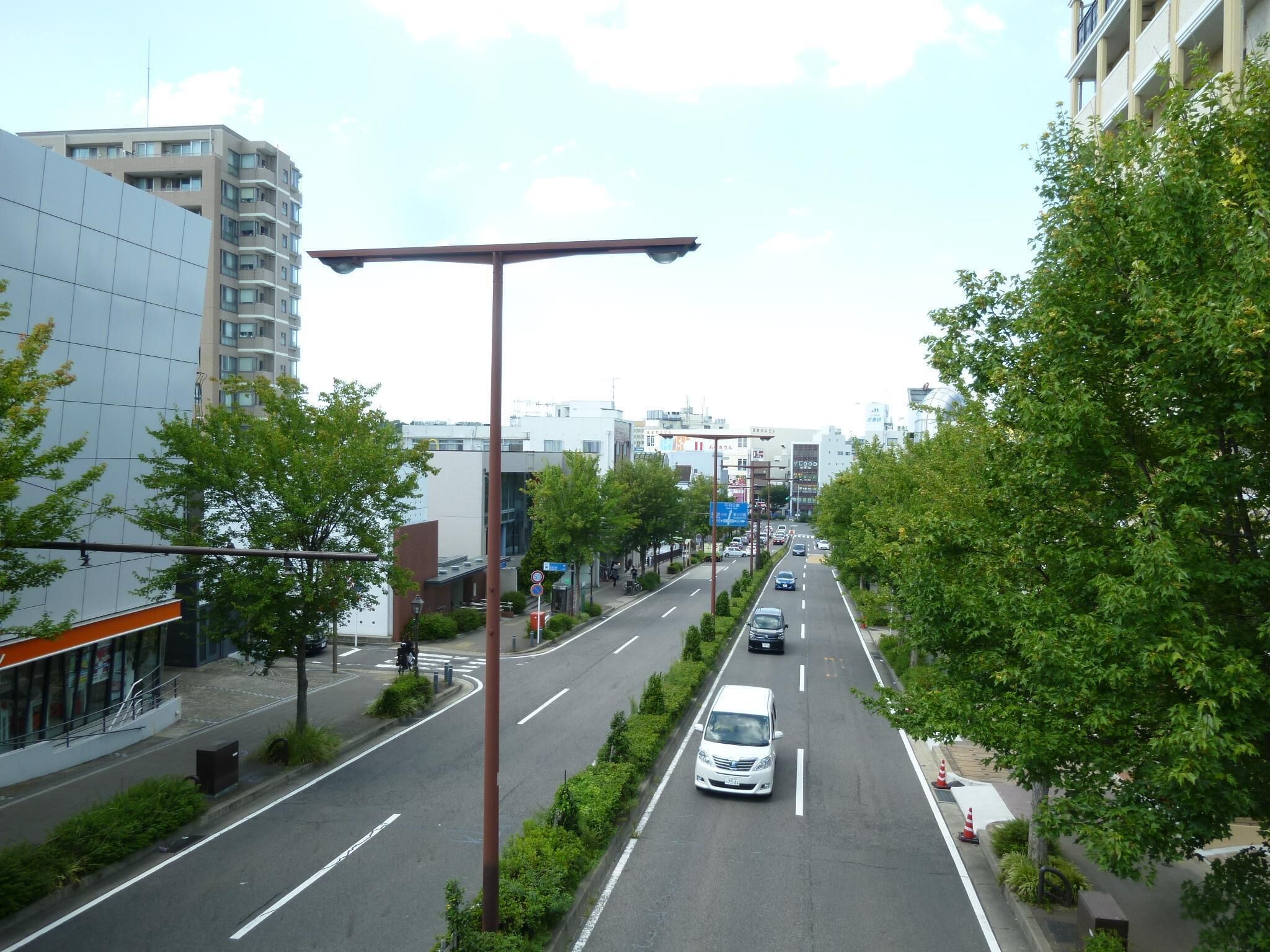 A multi-lane urban road with cars, a pedestrian crossing, and buildings on both sides.