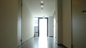 Ein langer, schmaler Korridor mit glattem Boden und weißen Wänden. Auf beiden Seiten befinden sich Türen, und ein offenes Ende des Korridors gibt einen hellen Raum mit einem Fenster frei.