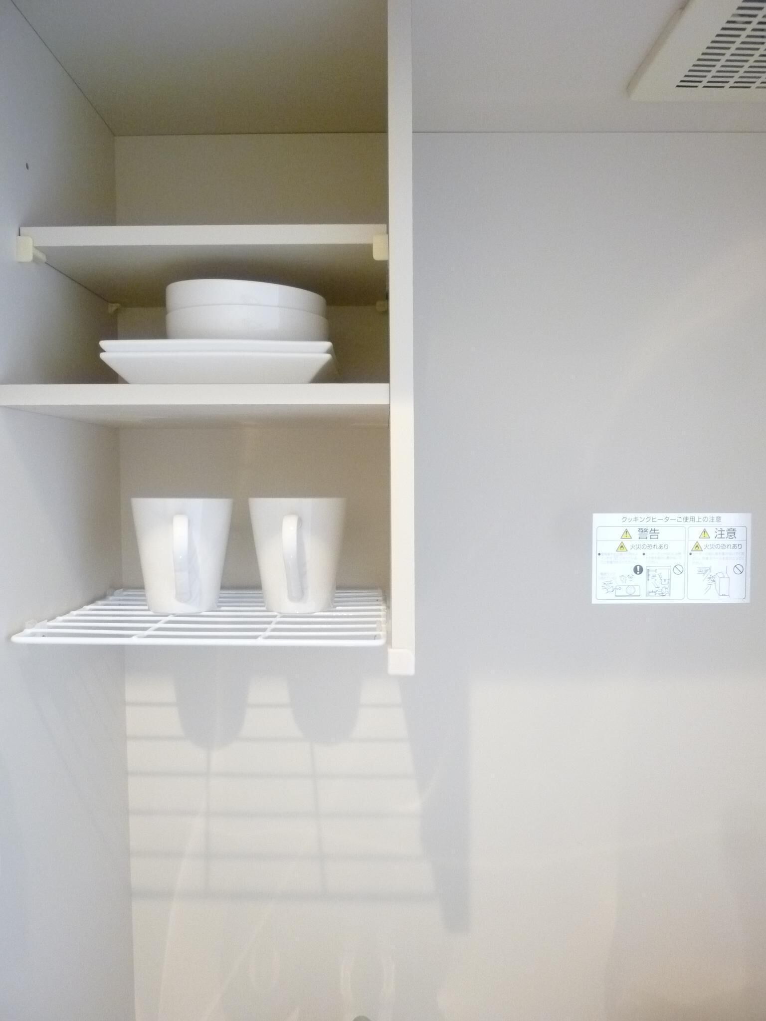 A kitchen with white shelves holding dishes and cups. There is a safety sign on the wall.