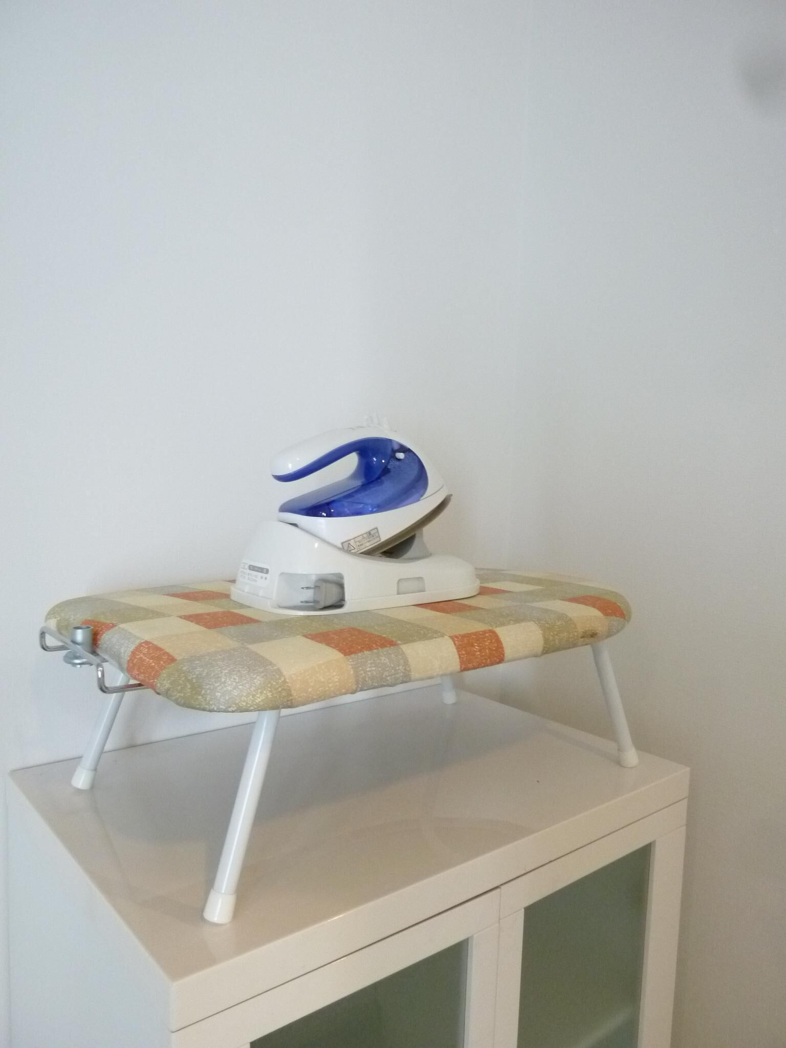 A compact ironing station with a quilted ironing board on a white cabinet.