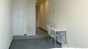 Habitación de hotel con una cama, un escritorio y una silla. Se ve una puerta que da a otra habitación.