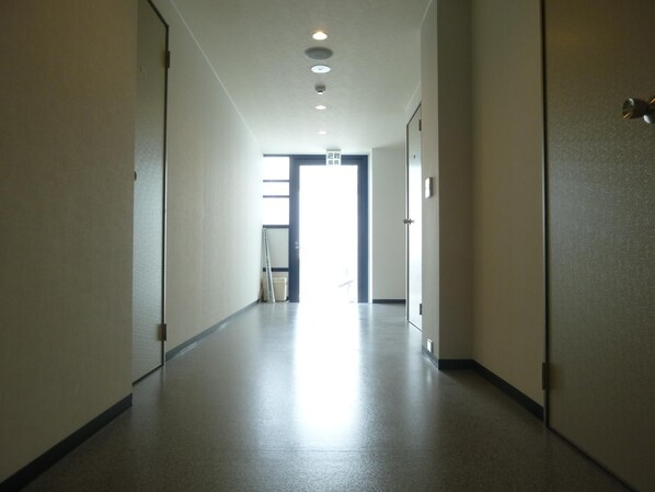 A long, narrow hallway with a smooth floor and white walls. There are doors on both sides, and a door at the end of the hallway is open, revealing a bright room with a window. - Nagoya Motoyama House F (Nagoya)