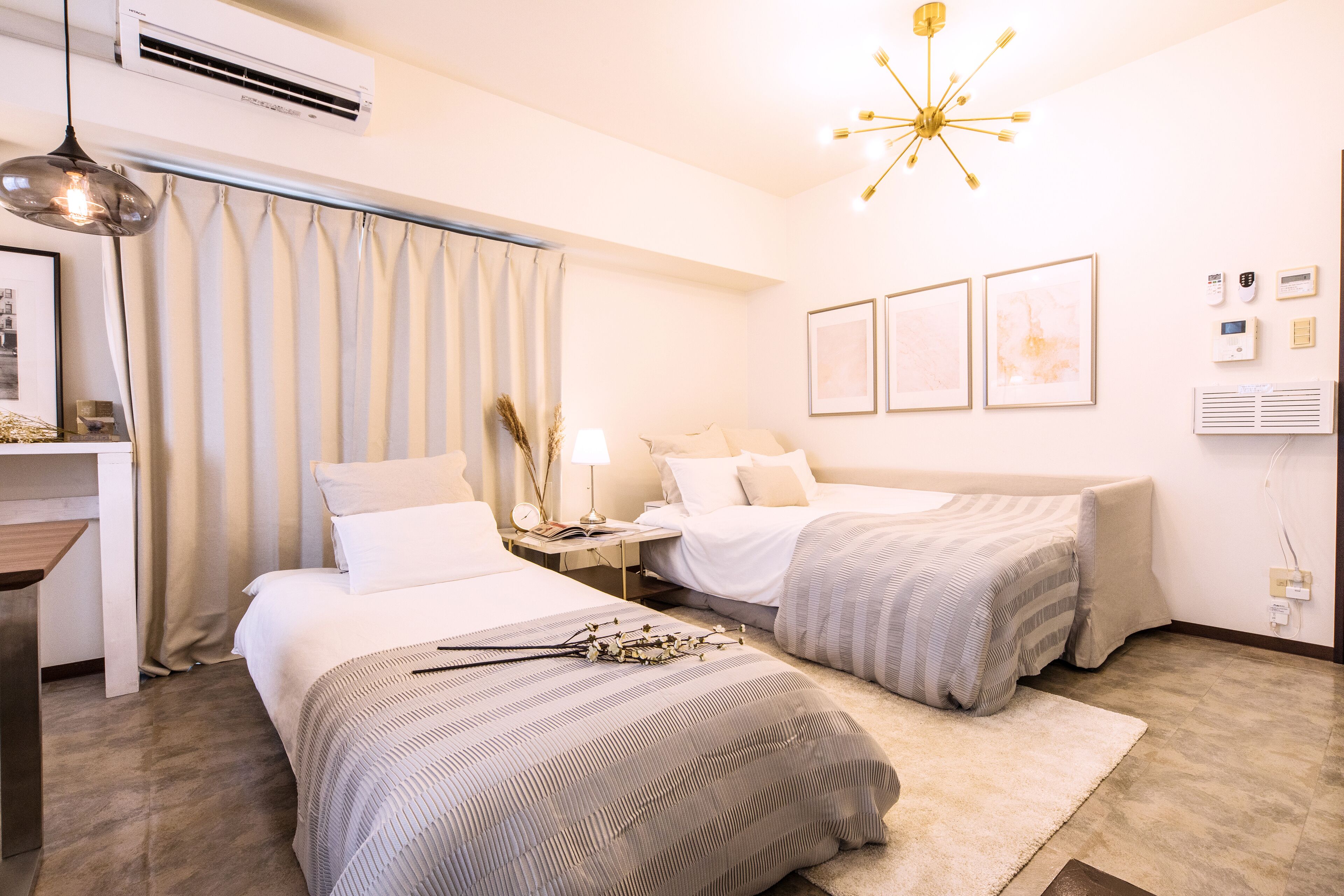 A hotel room with two beds, a desk, a lamp, and a modern chandelier.