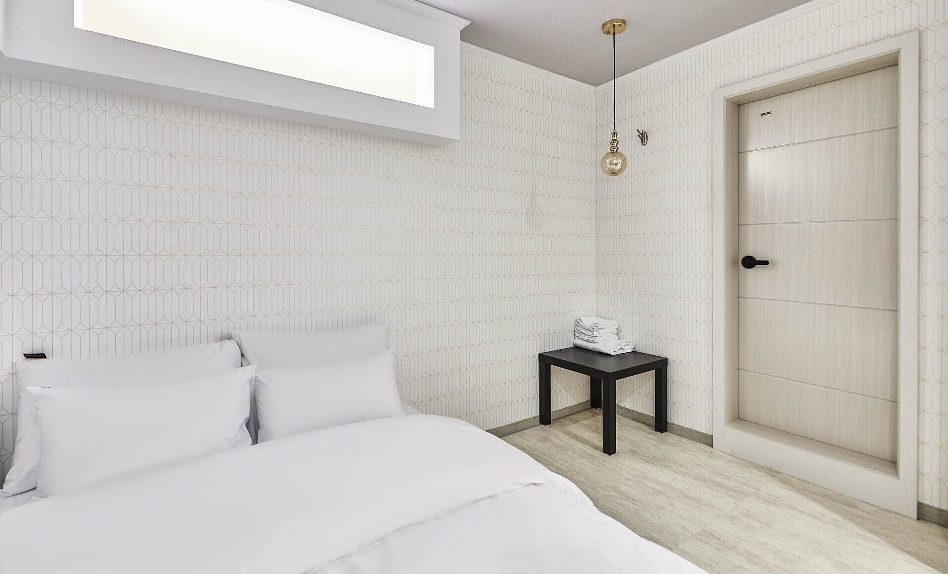 Un dormitorio moderno con una cama, una mesita con toallas, una puerta y una lámpara colgante.