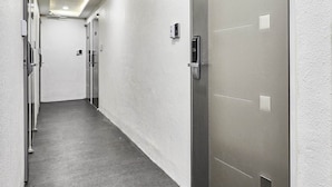 A hallway with a modern, minimalist design, featuring a grey carpet and white walls. There are doors on the right side, some with electronic keypads. - 30 month HOTEL (Seoul)