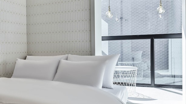A modern bedroom with a large bed, a small round table, and a view of a brick building through a large window. - 30 month HOTEL (Seoul)