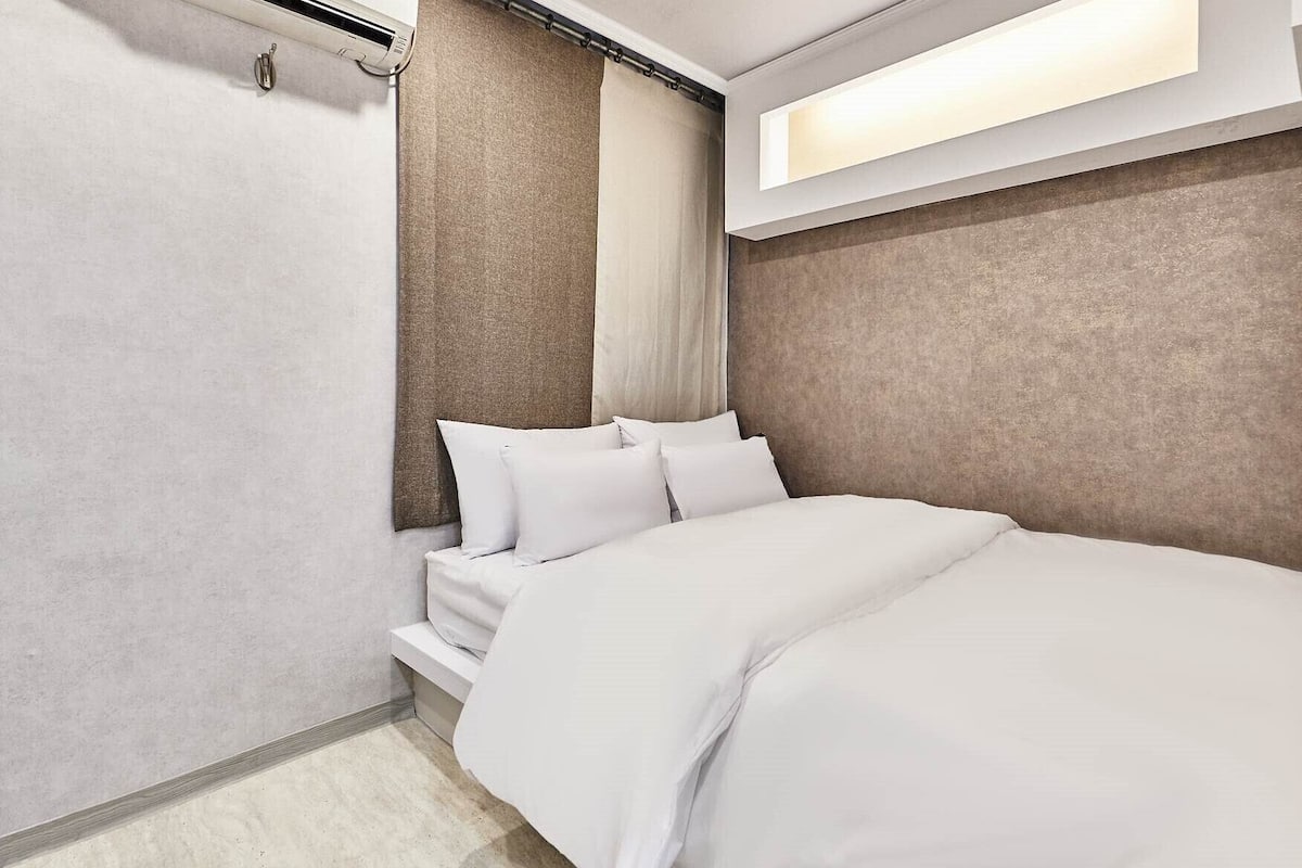 A modern hotel room with a large bed, a headboard with curtains, and a built-in light above the bed.