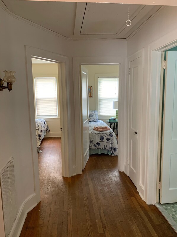 A hallway with wooden flooring leading to a bedroom with a bed and a window.
