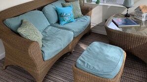 A cozy living room with a wicker sofa, matching ottoman, and a small side table with a lamp and book. - Residential Bungalow - Pet friendly, WiFi, Quiet Residential Area (Norfolk)