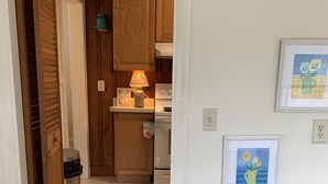 A cozy kitchen with wooden cabinets, a stove, and a trash can. There is a wicker chair and a framed picture on the wall. - Residential Bungalow - Pet friendly, WiFi, Quiet Residential Area (Norfolk)