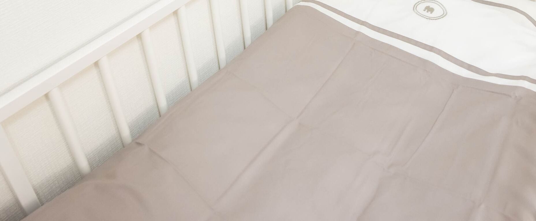 A beige bedspread on a white mattress with a visible button on the headboard.