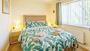 Een slaapkamer met een bed, nachtlampjes, een raam met gordijnen, een radiator en een hanglamp.