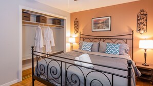Une chambre à coucher bien aménagée, avec un lit, des lampes de chevet, un ventilateur de plafond et un dressing où sont suspendus des vêtements.
