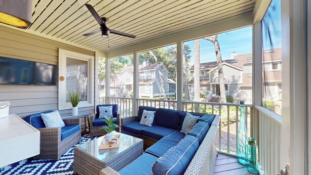 Eine überdachte Veranda mit Korbmöbeln, einem Deckenventilator und Blick auf Nachbarhäuser.