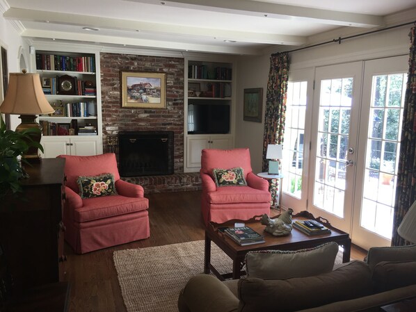 A living room with two red armchairs, a fireplace, a bookshelf, and a television.