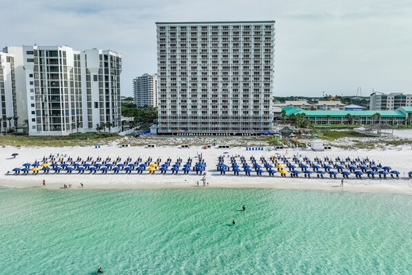 A beachfront hotel with multiple floors, a sandy beach with umbrellas, and clear turquoise water. - 19th Floor Pelican Beachfront with Ocean View (Destin)