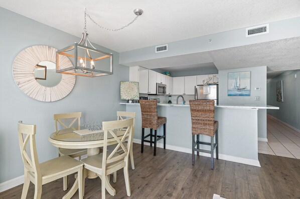 A modern kitchen with white cabinets, a central island, and a dining area with wicker chairs and a glass table.