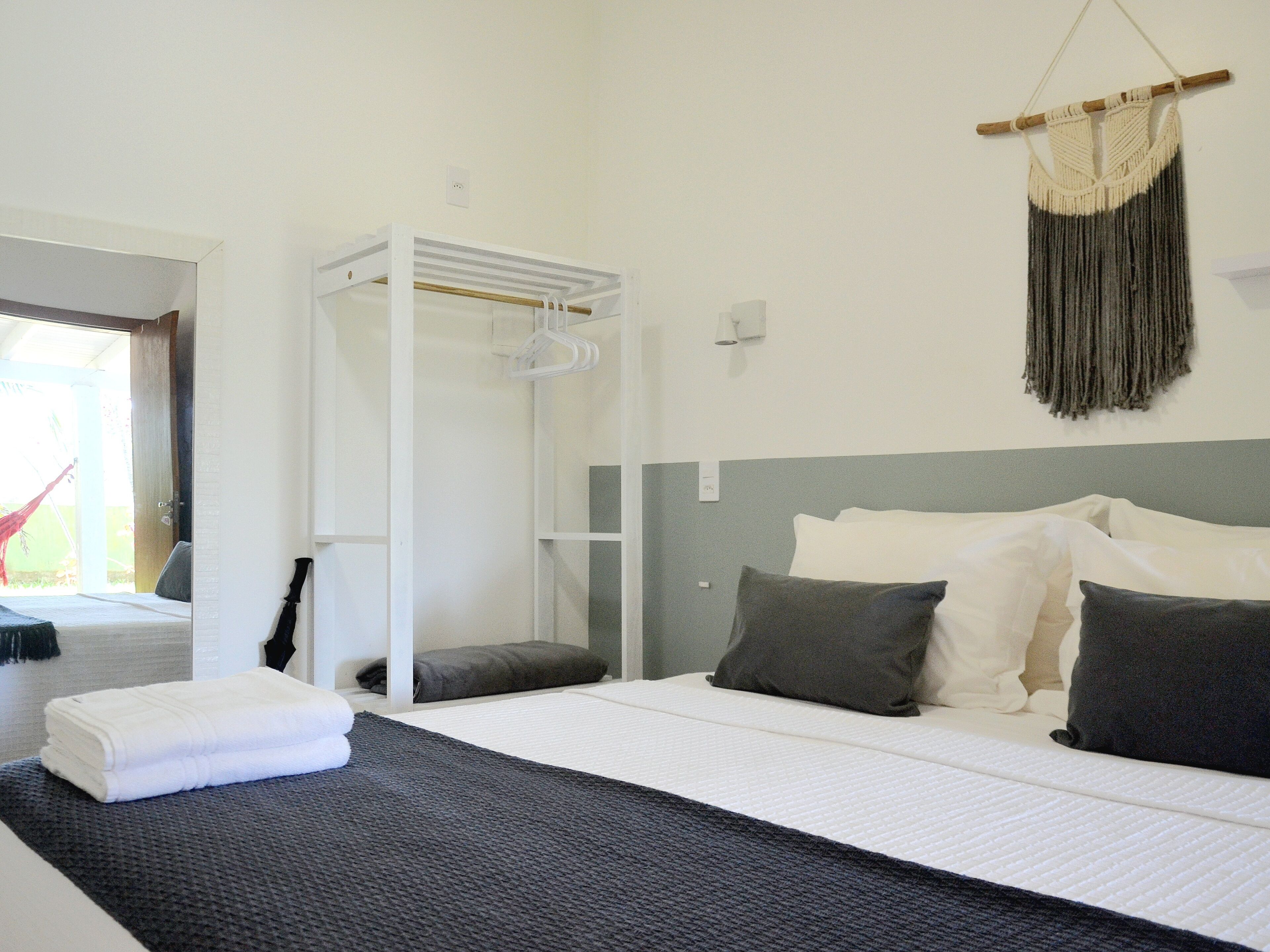 Een moderne slaapkamer met een bed, kussens, een hangende macramé decoratie en een witte garderobe.