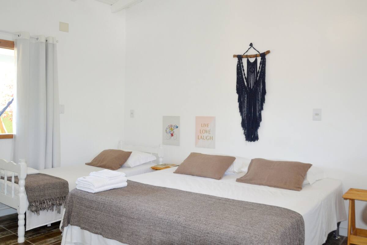 A bedroom with two beds, a wall-mounted macrame piece, and a 'Live Love Laugh' poster.