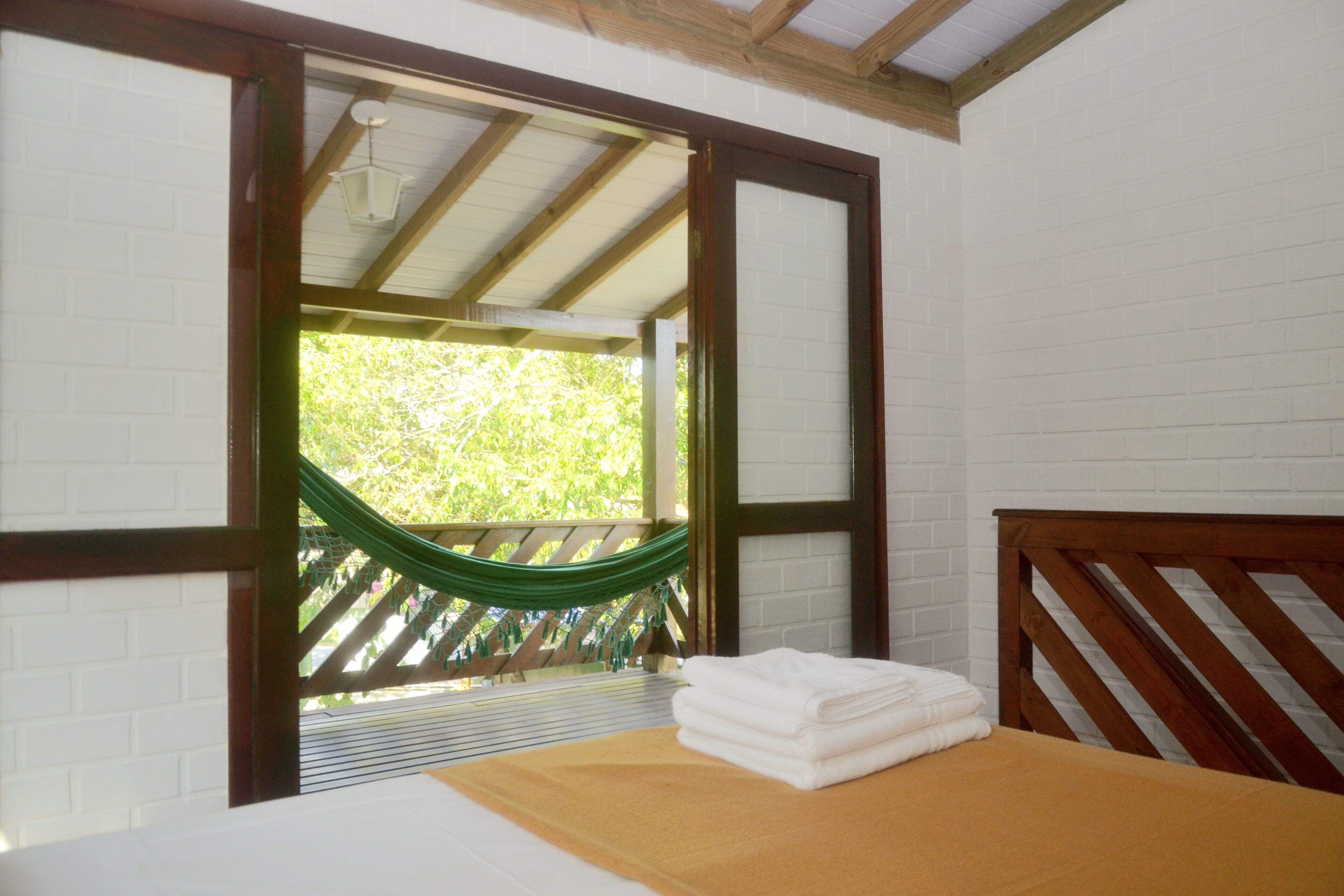 Una habitación con una cama, cabecera de madera, una hamaca verde y vistas al exterior con vegetación.