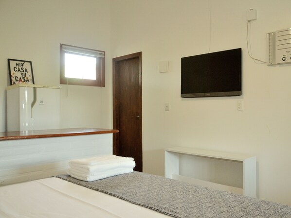 A hotel room with a bed, a TV mounted on the wall, a small window, and a minibar.