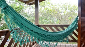 A hammock hanging on a wooden deck with a view of trees in the background. - Pousada la Boheme (Palhoça)