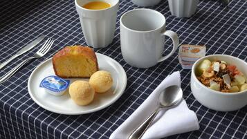 Een ontbijtsetting met een bord eten, een kop koffie, een kom ontbijtgranen en een lepel op een geruit tafelkleed.