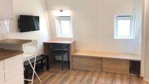 A compact room with a desk, chair, and a TV mounted on the wall. There are two windows providing natural light. - Brand new studio located in the center of Paris (Paris)