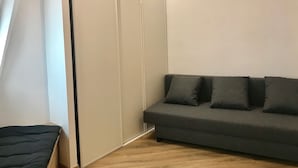 A room with a grey sofa, a wooden floor, and a white wall with a sliding door. - Brand new studio located in the center of Paris (Paris)