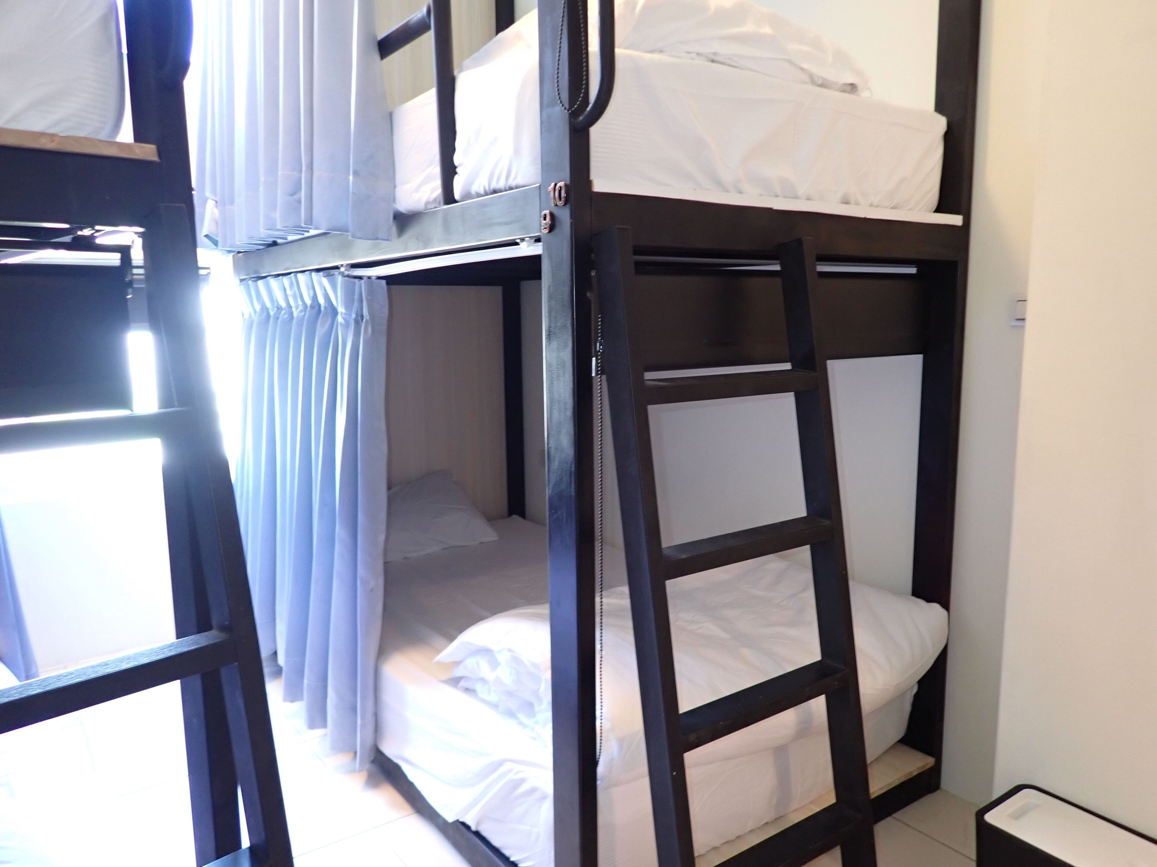 A bunk bed room with a ladder, white bedding, and curtains.