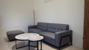 A modern living room with a grey sofa, two round tables, and a wooden coat rack. - Ji Guang Dive Resort - Hostel (Lyudao)