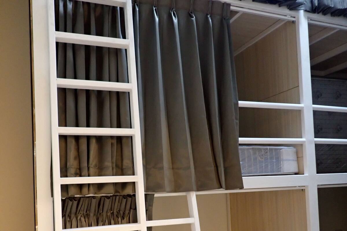 A bunk bed with a ladder, a shelf with folded blankets, and a storage unit with a plastic cover.