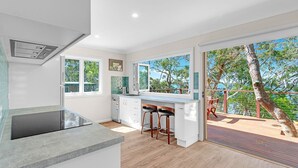A modern kitchen with a large window, a built-in oven, and a bar area with stools. - Banksia House allows you to surround yourself with nature in this serene piece of paradise (Sanctuary Point)
