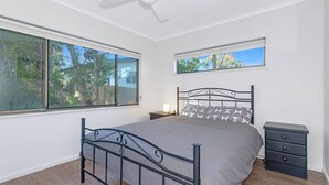 A bedroom with a bed, nightstand, dresser, and large windows with views of trees. - Banksia House allows you to surround yourself with nature in this serene piece of paradise (Sanctuary Point)