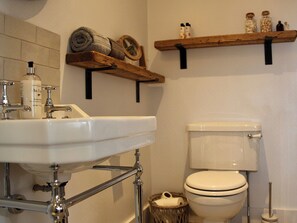 A bathroom with a white sink, a toilet, and wooden shelves above the toilet.