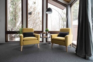 Relax in a serene space with a view of the surrounding trees, featuring a comfortable seating area with a table and lamp.