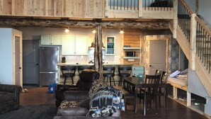 A spacious living area with a high ceiling, wooden beams, a cozy couch, a dining table, and a kitchen in the background. - Lookout cabin (Kamiah)
