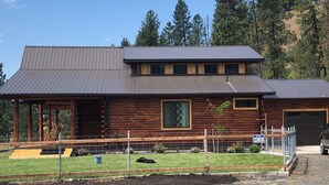 A two-story log cabin with a metal roof, a fenced yard, and a gravel driveway. - Lookout cabin (Kamiah)