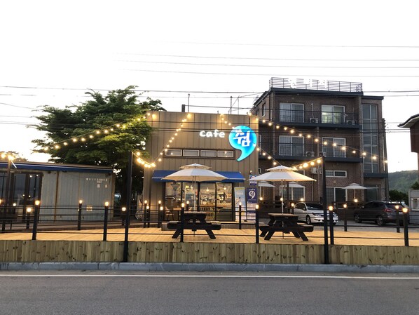 A cafe with outdoor seating, a sign with foreign script, and a building with balconies in the background. - Jebudo Yeonliji Pension (Hwaseong)