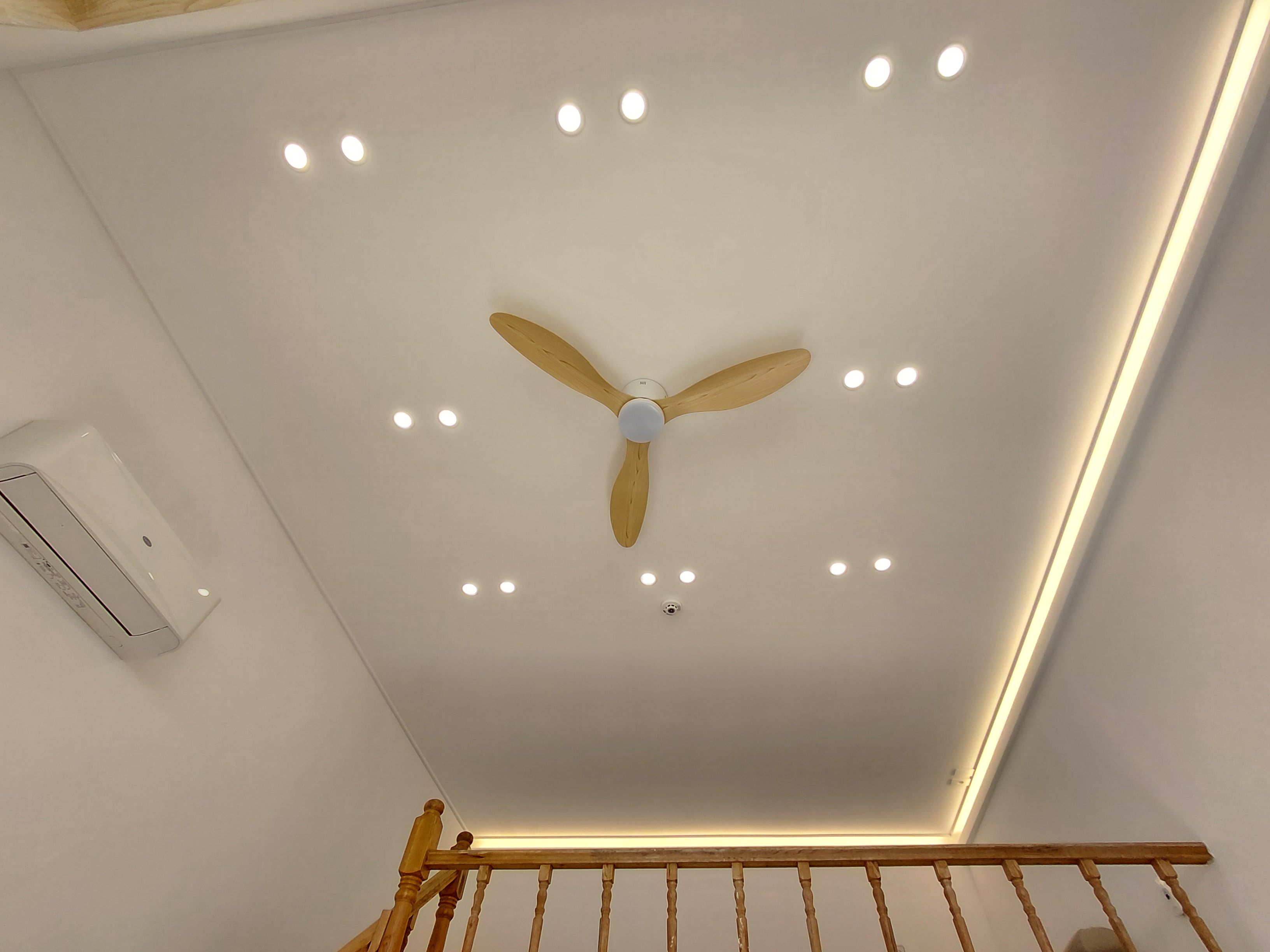 Un plafond doté d’un ventilateur central, d’un éclairage encastré et d’une rambarde en bois.