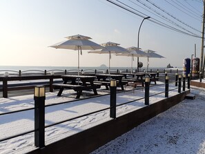 A snow-covered promenade with picnic tables and umbrellas, overlooking a body of water. - Jebudo Yeonliji Pension (Hwaseong)
