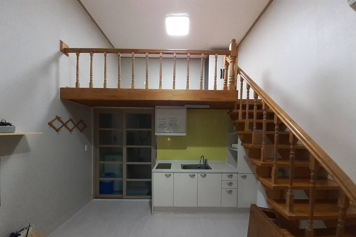 A compact kitchen with a wooden staircase leading to a loft area.
